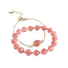 Pink strawberry quartz beaded bracelet with gold chain on white background