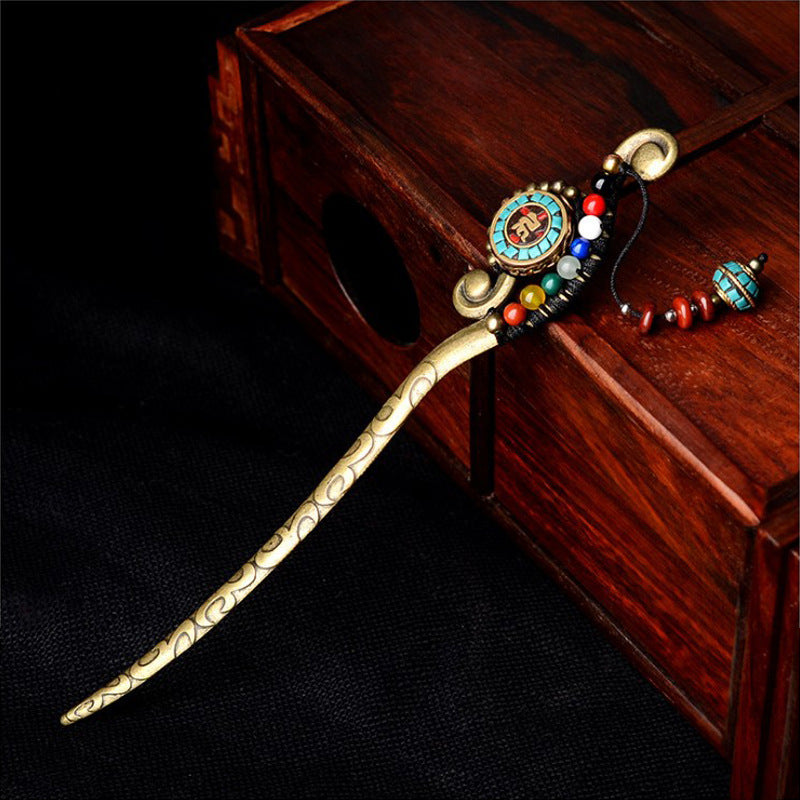 A vintage gold-tone Tibetan hairpin with colorful beads and a tassel resting on a wooden box.