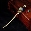 A vintage gold-tone Tibetan hairpin with colorful beads and a tassel resting on a wooden box.