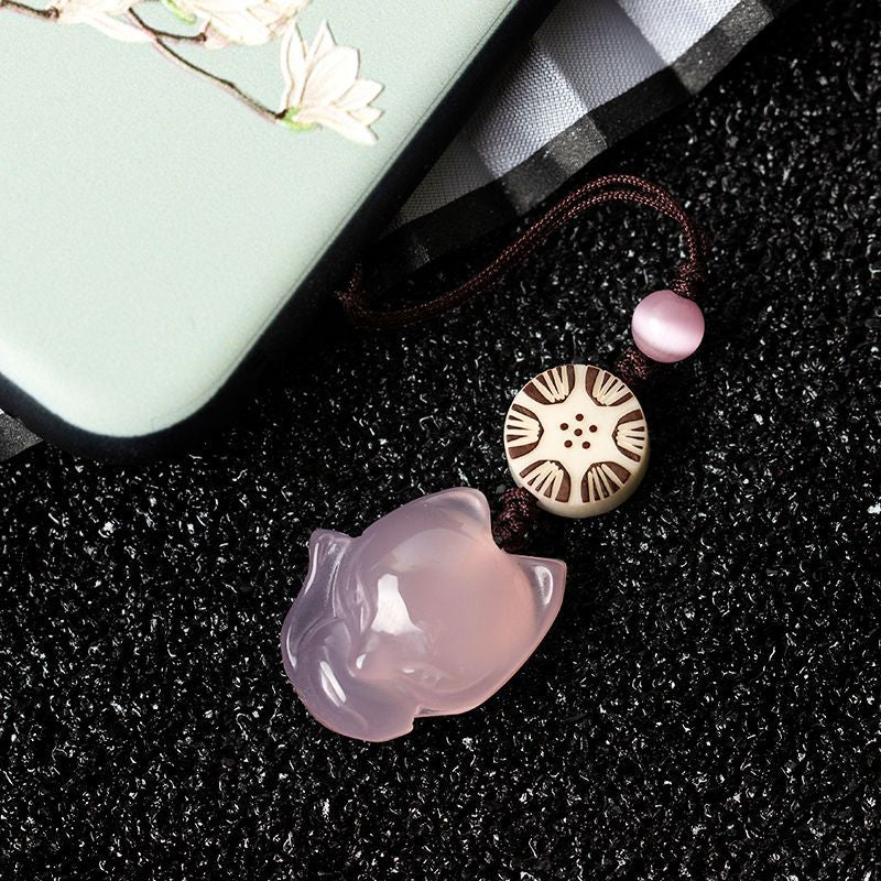 Pink chalcedony fox phone charm with brown cord and wooden bead on black background