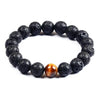 A beaded bracelet made of black lava rock stones with one central golden brown tiger eye bead on a white background