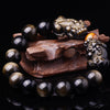 Two gold-tone Pixiu charms on a black obsidian beaded bracelet with a tiger eye bead