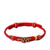 Close up of a red braided bracelet with a gold tone peace knot centerpiece