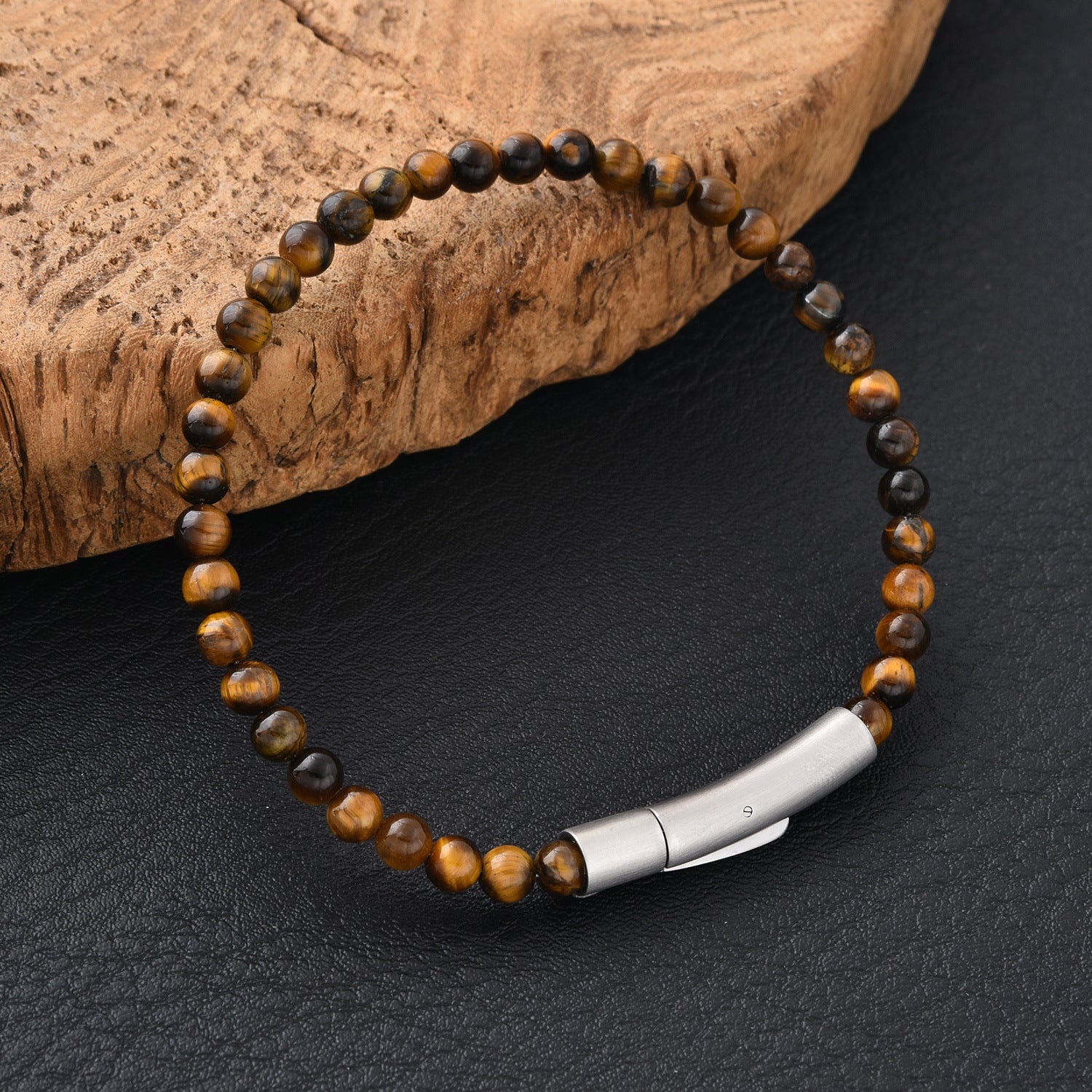 Close up of a brown tiger eye bead bracelet with a silver metal bar on a dark surface