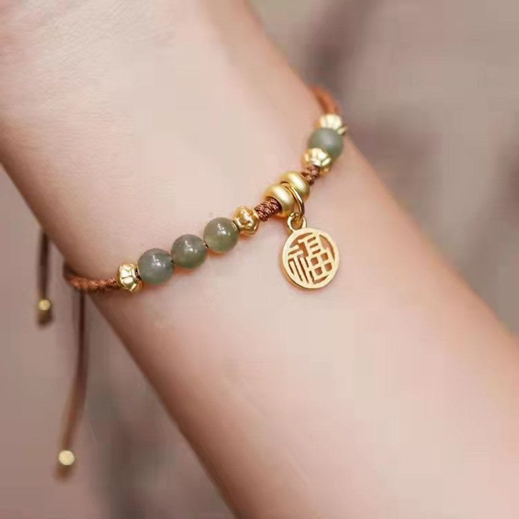 Close up of a jade beaded bracelet with a gold Fu charm on a wrist