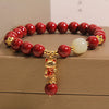 Close-up of a red cinnabar beaded bracelet with a gold lucky cat charm on a box