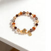 Close-up view of a tiger eye and pearl beaded bracelet with a gold horse charm on a white surface