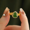 Close up of a gold tone ring with a green gourd shaped stone held between fingers