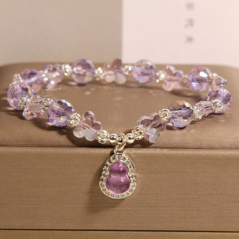 Close-up of a purple crystal bracelet with butterfly beads and a gourd pendant on a gold box.