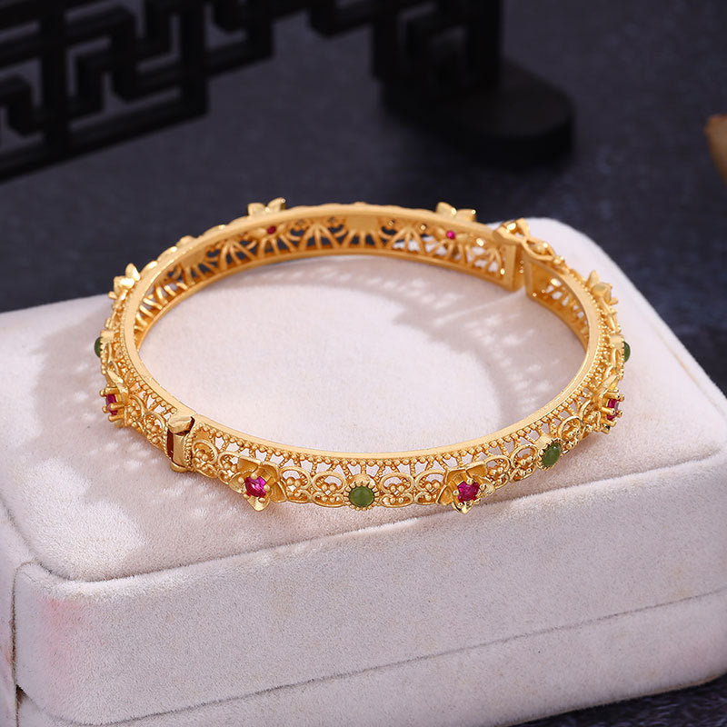 Gold plated copper bangle with hollow floral design and colored stones in a white box