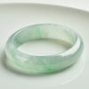 A natural jade bangle bracelet with light green and white colors on a white background