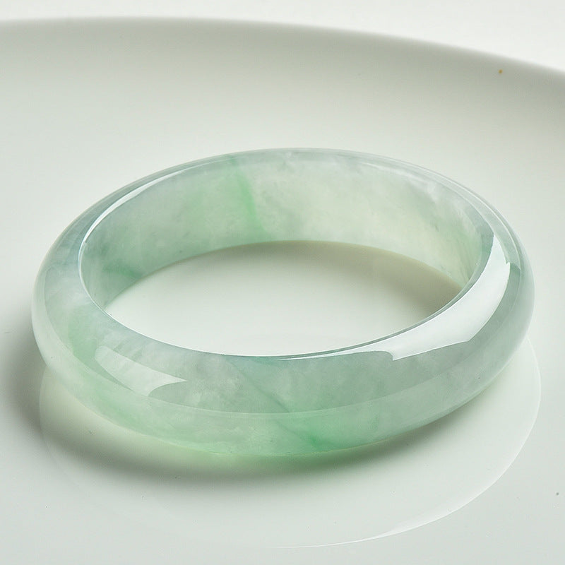 A natural jade bangle bracelet with light green and white colors on a white background