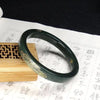 Dark green natural Hetian jade bangle with gold-tone floral pattern resting on a wooden stand