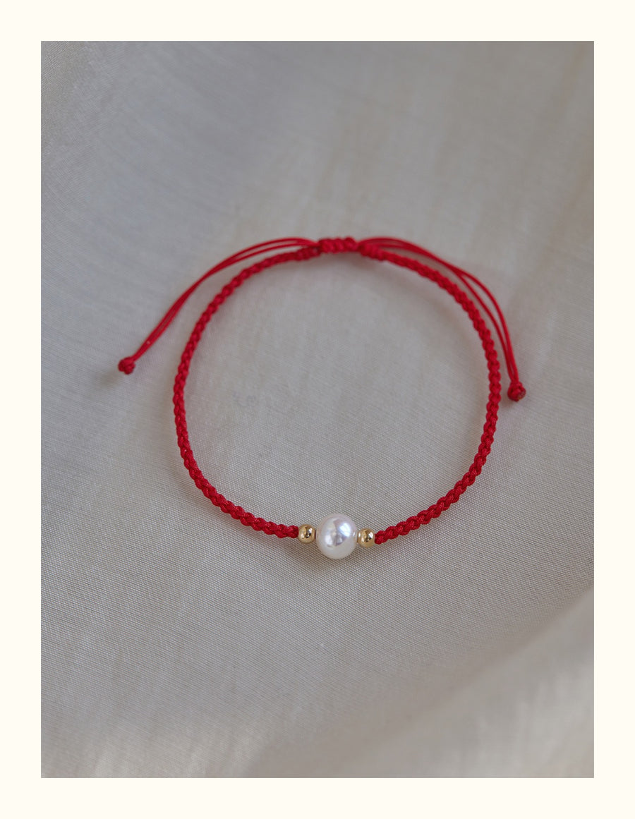 Close up of a wrist wearing a red braided bracelet with a single white pearl bead