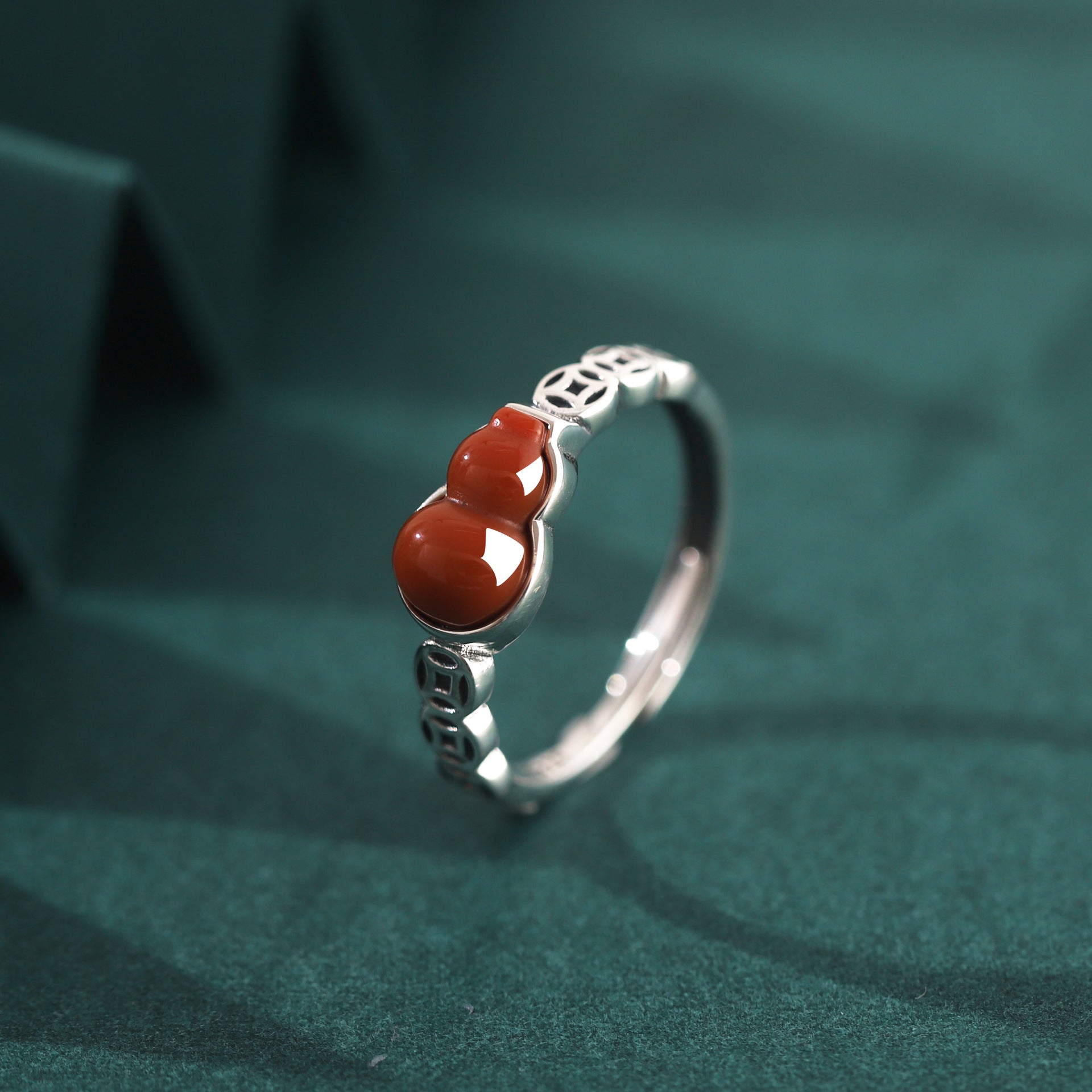 Close up of a sterling silver ring with a red gourd shaped stone and coin details on a green background