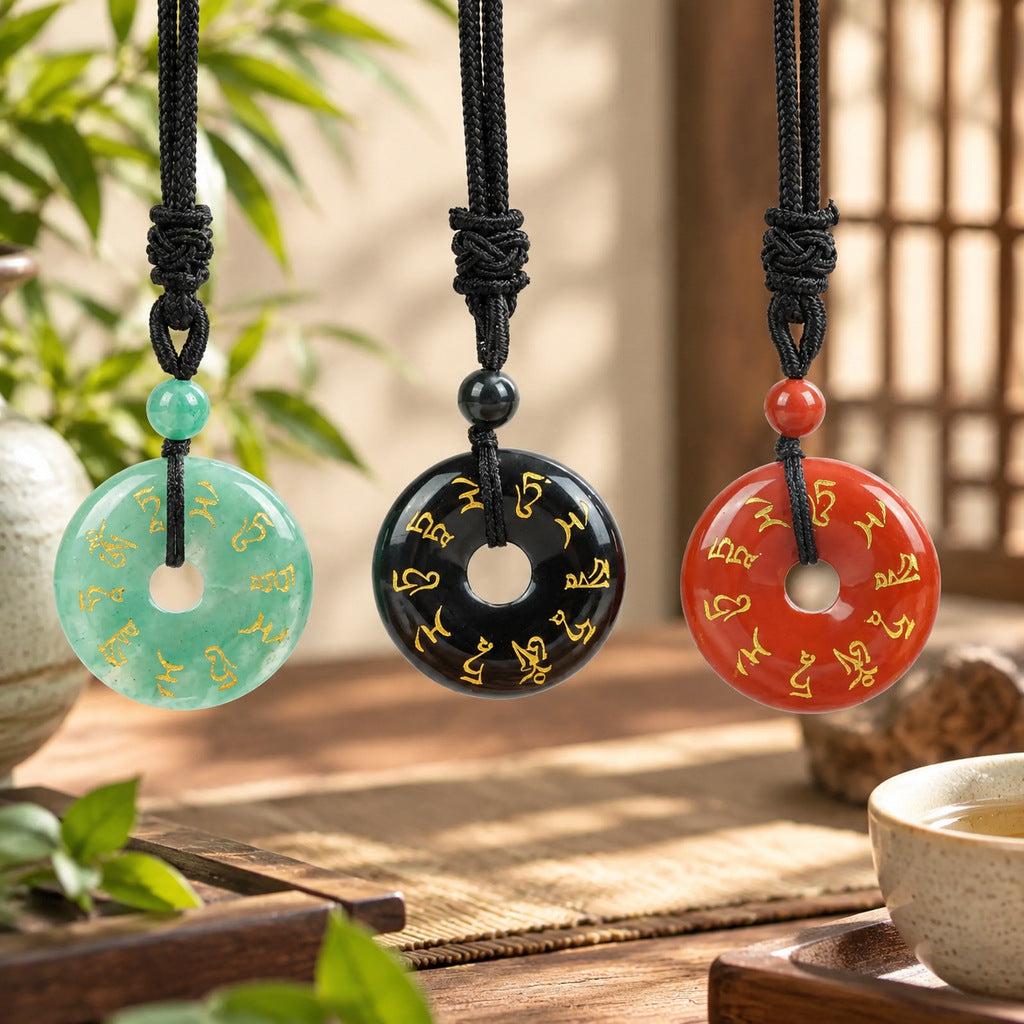Three natural stone peace buckle pendants in green, black, and red hanging on black cords