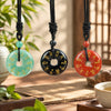Three natural stone peace buckle pendants in green, black, and red hanging on black cords