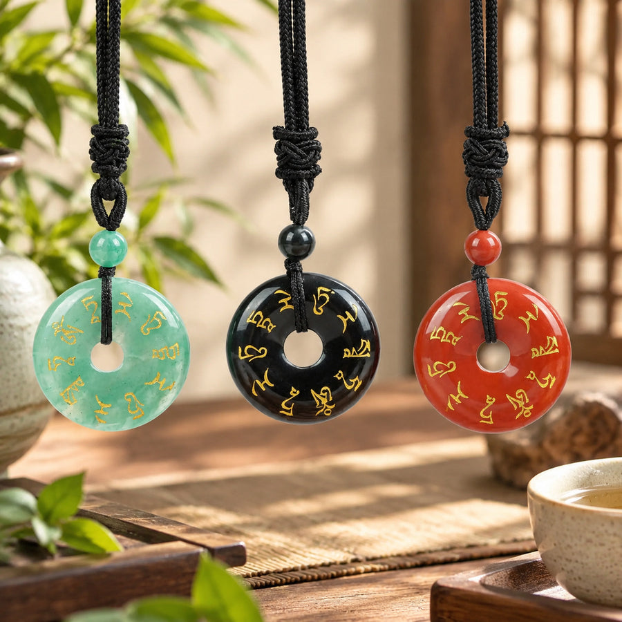 Three natural stone peace buckle pendants in green, black, and red hanging on black cords