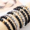 Stack of matte black lava rock and white howlite bracelets with metal and skull charms on a wrist