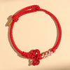 A close-up of a red braided cord bracelet with a decorative knot and white beads.
