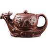 A brown clay teapot shaped like a dragon boat held in a hand against a dark background