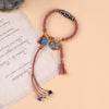 Close-up of a red and orange braided bracelet with a black and white Dzi bead and tassel charms.