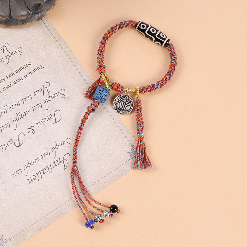 Close-up of a red and orange braided bracelet with a black and white Dzi bead and tassel charms.