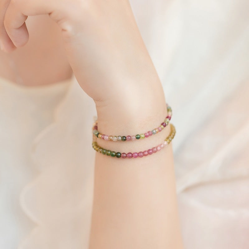Wrist wearing a thin multicolor beaded tourmaline bracelet with gold clasp