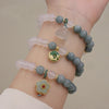 Wrist wearing a beaded bracelet with green and white stones and a gold flower charm