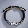 Close up of a black braided bracelet with a silver tone cylinder charm featuring cloud patterns