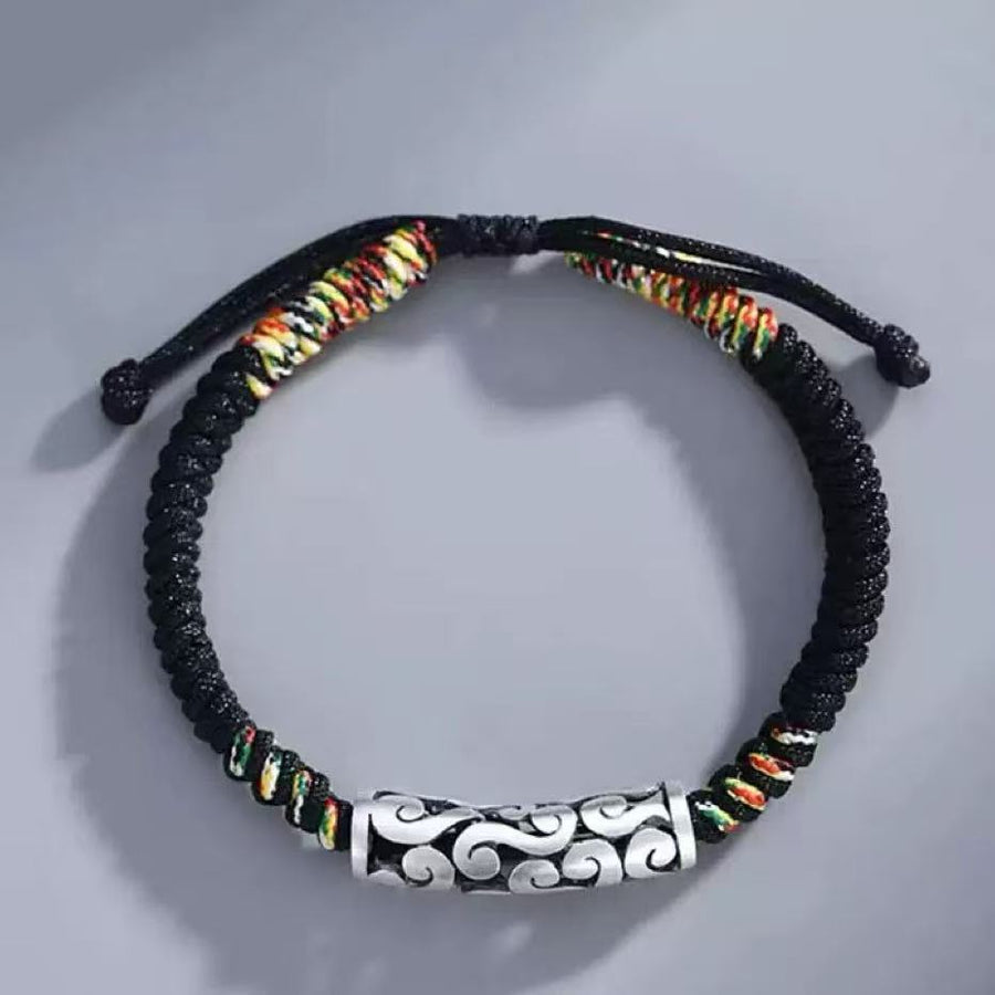 Close up of a black braided bracelet with a silver tone cylinder charm featuring cloud patterns