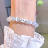 A wrist wearing a white cat's eye bead bracelet with a central silver-tone Pixiu charm.