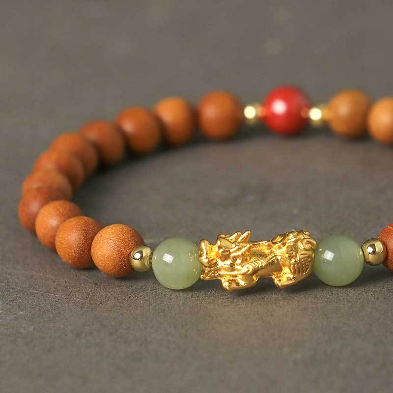 Close-up of a wooden bead bracelet with a gold-tone Pixiu charm and green jade beads on a dark surface.