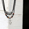 Silver-tone anchor pendant hanging from a black braided cord with beads.