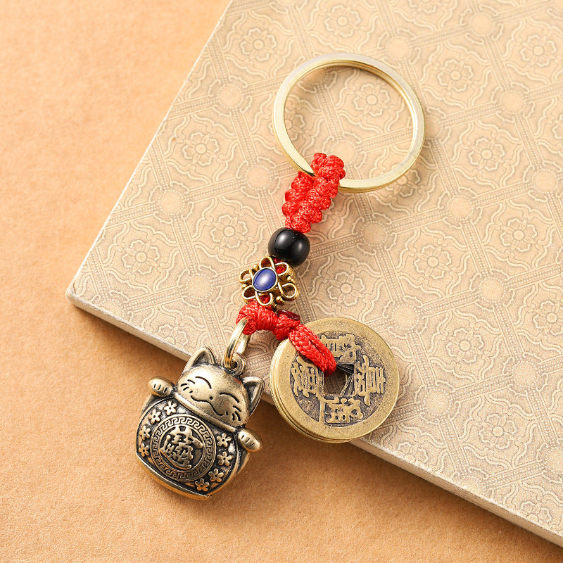 Close up of a brass lucky cat keychain with red cord and blue beads