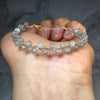 Close-up of a handmade natural moonstone bracelet with gold-tone wire wrapping held in a hand