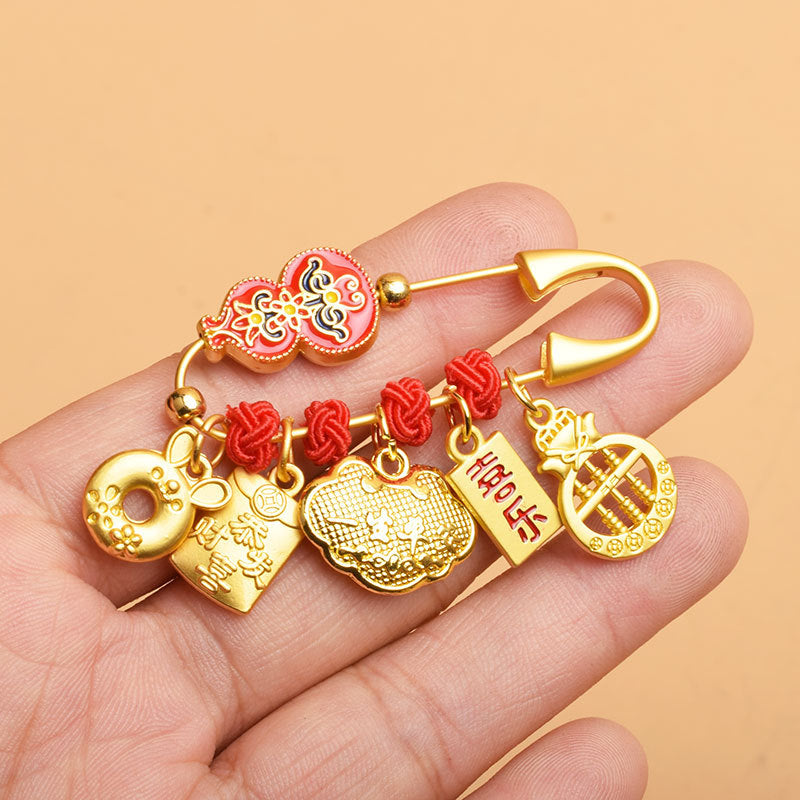 Gold-tone safety pin brooch with red gourd and hanging charms held in hand
