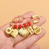 Gold-tone safety pin brooch with red gourd and hanging charms held in hand
