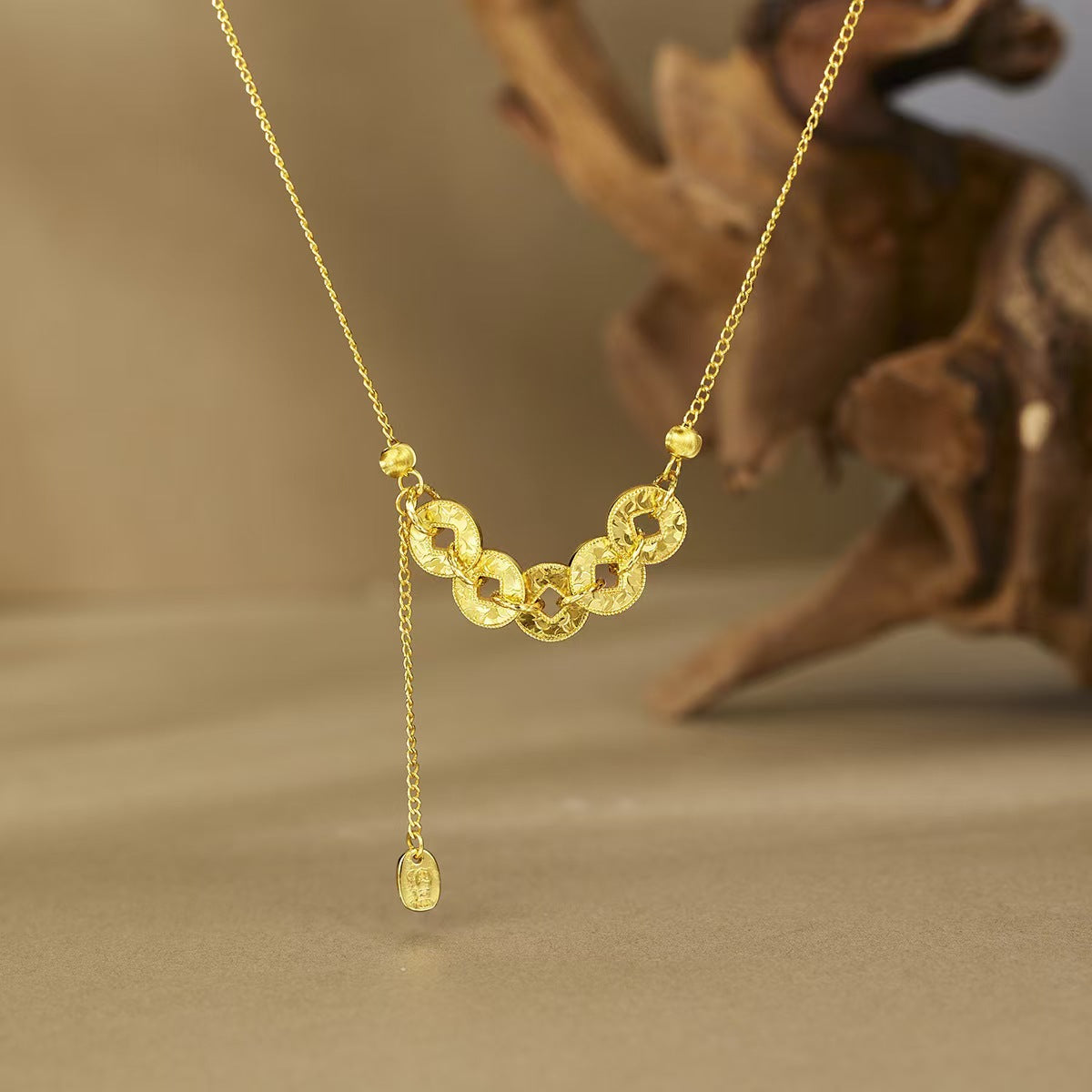 Close up of a gold plated sterling silver necklace with five coin charms on a beige surface.