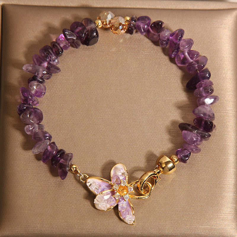Close up of an amethyst gravel bracelet with a gold-tone flower charm on a beige background