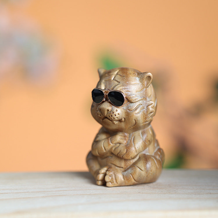 Close up of a small green sandalwood tiger carving wearing sunglasses on a wooden surface