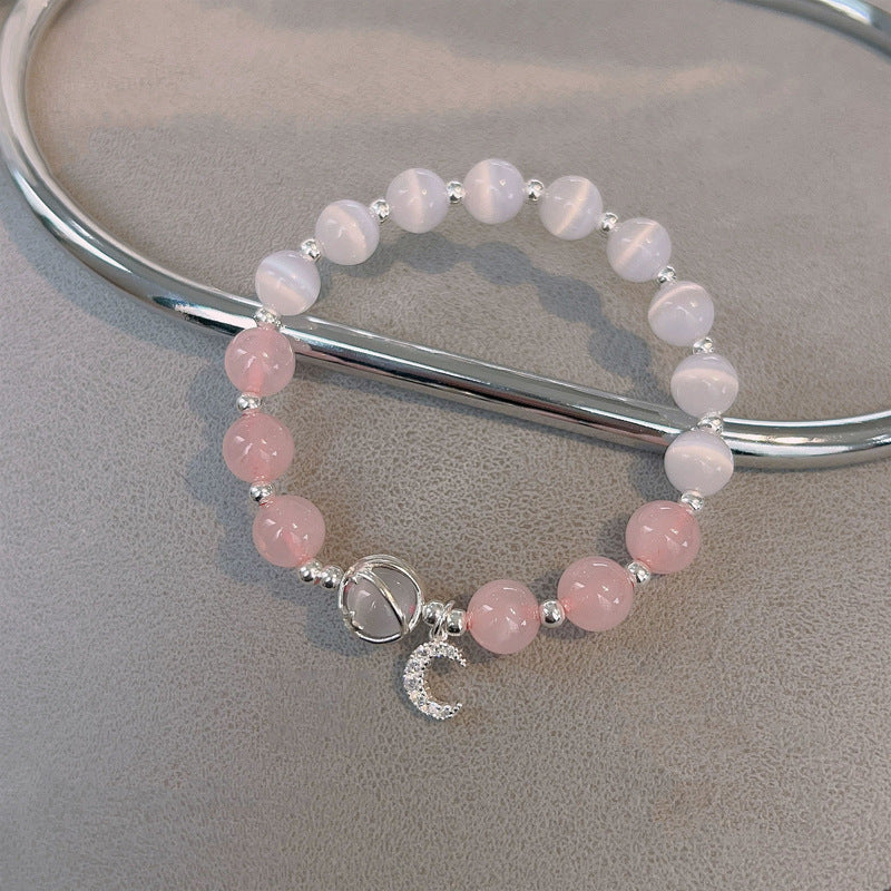 Pink rose quartz and white cat's eye bead bracelet with moon charm on grey surface