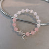 Pink rose quartz and white cat's eye bead bracelet with moon charm on grey surface