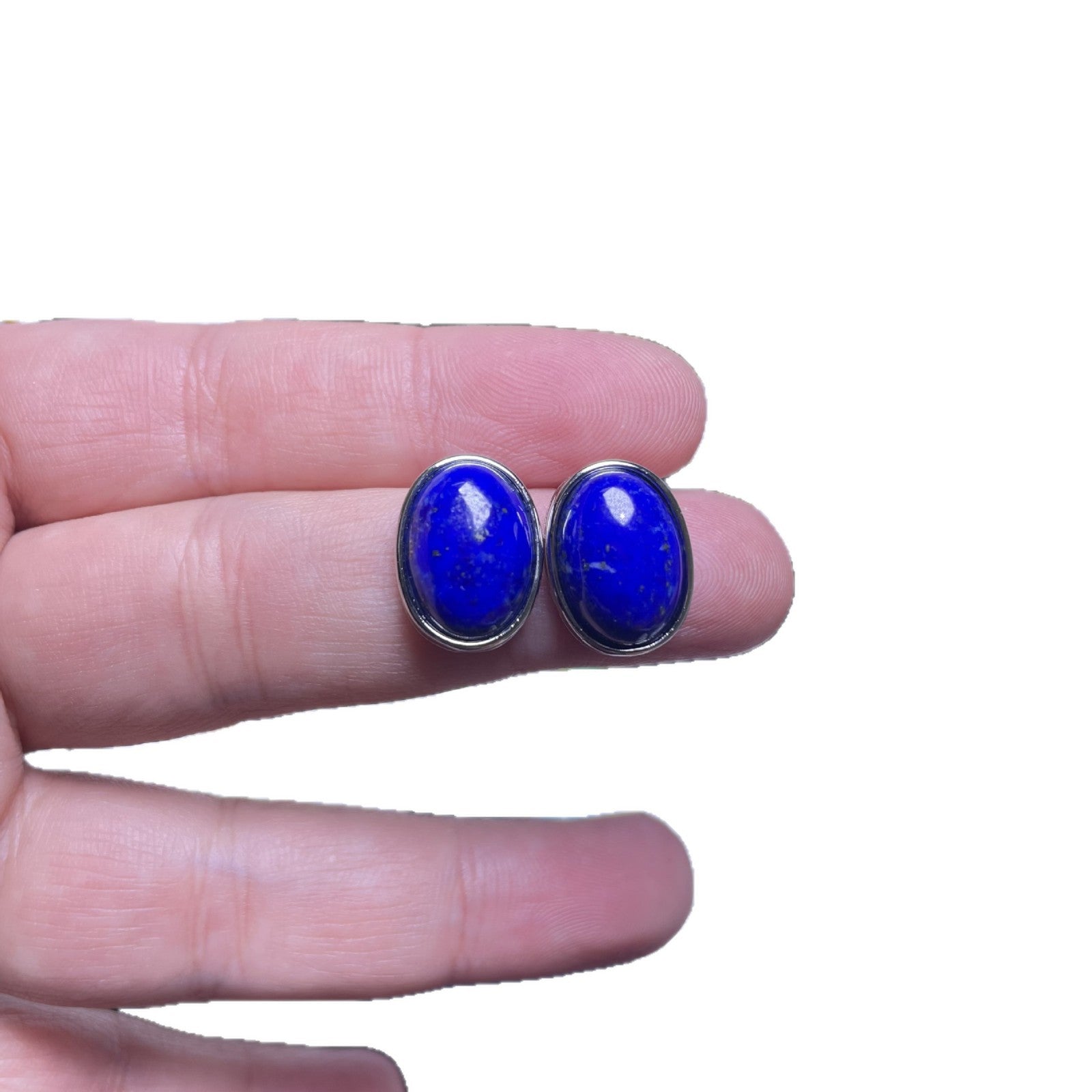 A pair of oval blue lapis lazuli stud earrings held between fingers
