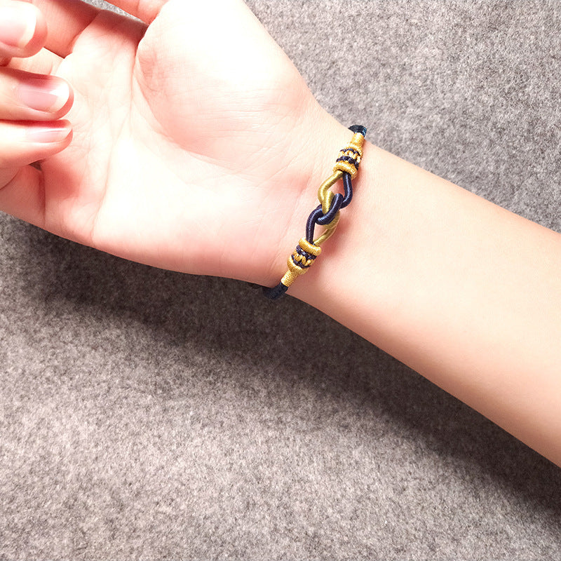 A wrist wearing a blue and gold handmade braided bracelet with a central knot design.