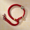 Close up of a red braided string bracelet with a silver and gold tone bead charm