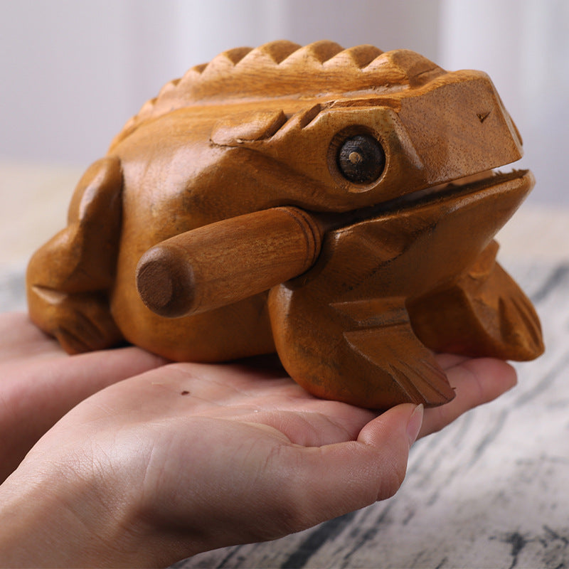 A hand holding a carved wooden frog with a ridged back and a small rubbing stick.