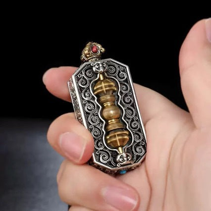 Close up of a rectangular silver tone pendant with a brass vajra center held in hand