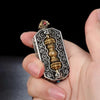 Close up of a rectangular silver tone pendant with a brass vajra center held in hand