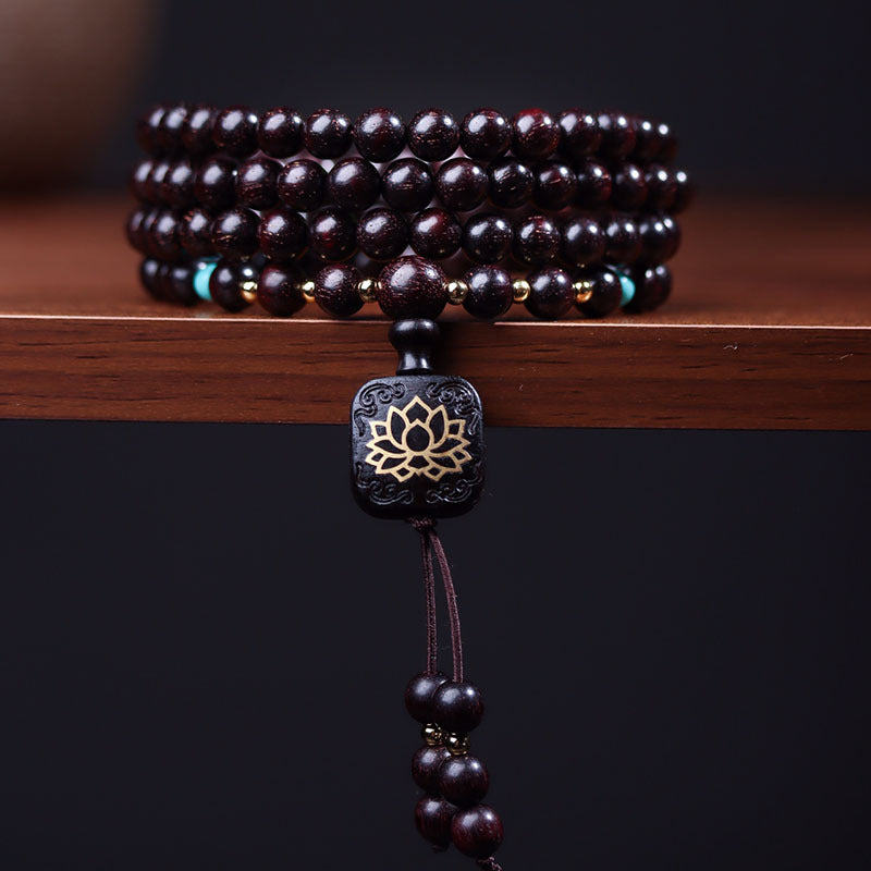 Red sandalwood 108 bead mala bracelet with a lotus pendant resting on a wooden surface